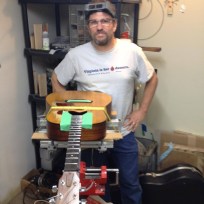 Fret boss wearing work goggles, standing beside a guitar undergoing major surgery.